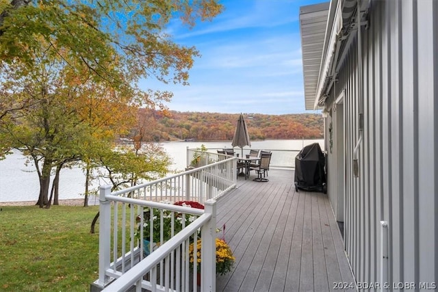 wooden terrace featuring a grill, a lawn, and a water view