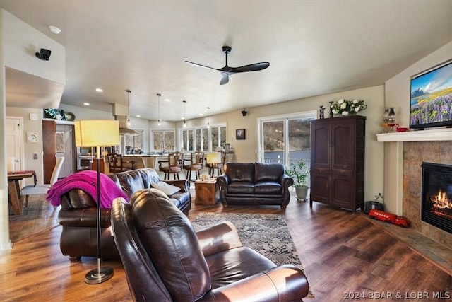 living room featuring a tiled fireplace, ceiling fan, and dark wood-type flooring