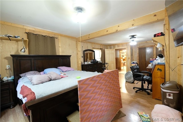 bedroom with beam ceiling, wooden walls, and light wood-type flooring