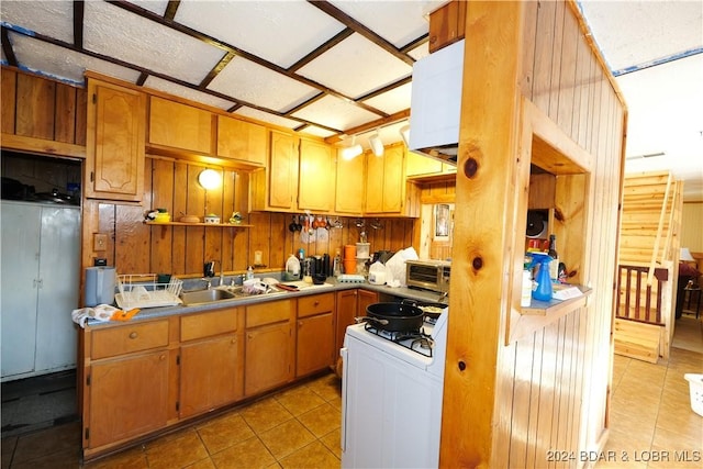 kitchen featuring light tile patterned floors, sink, gas range gas stove, and wood walls