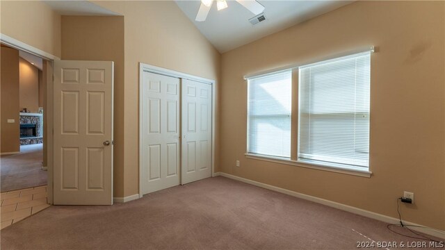 unfurnished bedroom featuring ceiling fan, light colored carpet, vaulted ceiling, and a closet