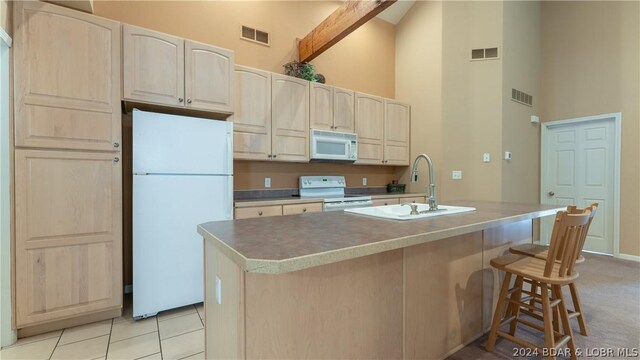 kitchen with white appliances, a kitchen island with sink, light tile patterned floors, high vaulted ceiling, and sink