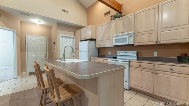 kitchen featuring sink, white appliances, a kitchen bar, light tile patterned flooring, and a center island with sink