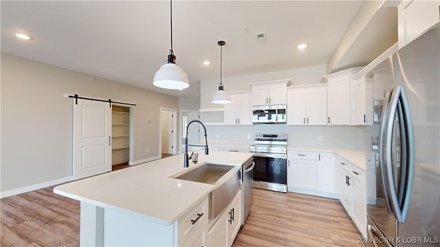 kitchen featuring white cabinets, appliances with stainless steel finishes, pendant lighting, and a barn door