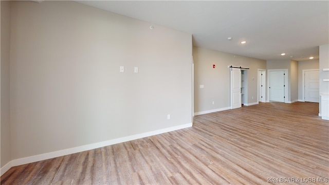 unfurnished room with a barn door and light hardwood / wood-style flooring