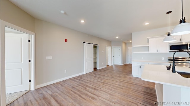 kitchen with pendant lighting, white cabinetry, appliances with stainless steel finishes, a barn door, and light hardwood / wood-style floors