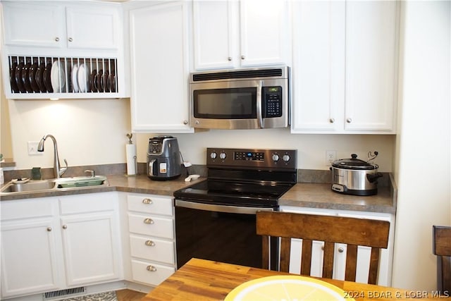 kitchen featuring stainless steel microwave, visible vents, black electric range oven, white cabinets, and a sink