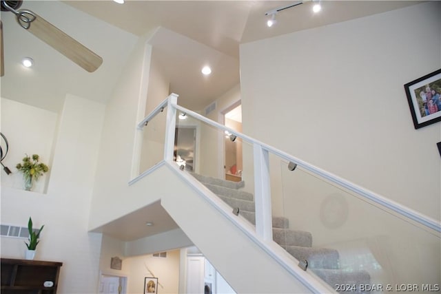 staircase featuring rail lighting, a high ceiling, visible vents, and recessed lighting