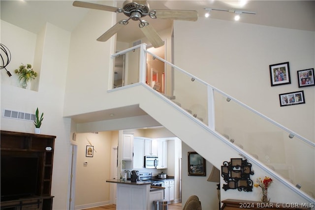 staircase with ceiling fan, sink, and high vaulted ceiling