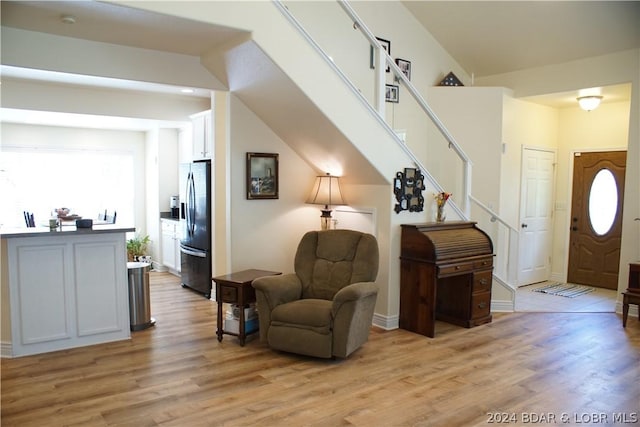 living area featuring light wood-style floors, baseboards, and stairs