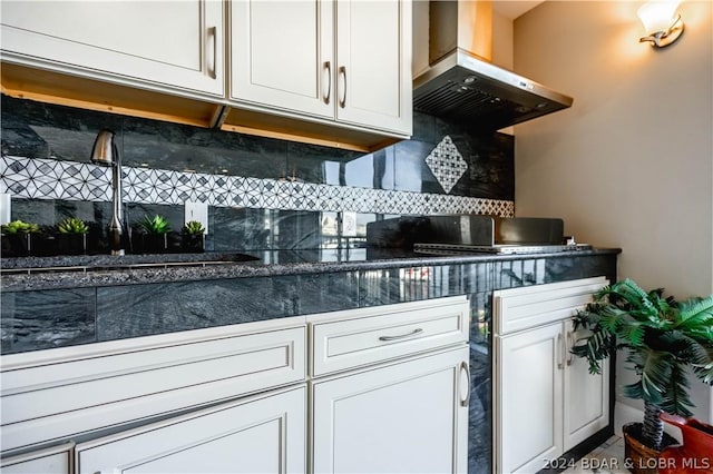 kitchen with backsplash, white cabinetry, wall chimney range hood, and sink