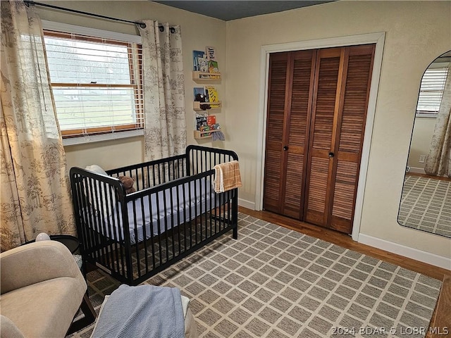 bedroom featuring a nursery area, a closet, multiple windows, and hardwood / wood-style flooring