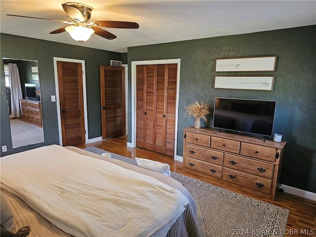 bedroom with ceiling fan, two closets, and wood-type flooring