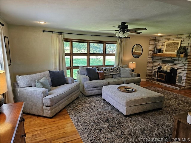 living room with ceiling fan, a wood stove, and wood-type flooring