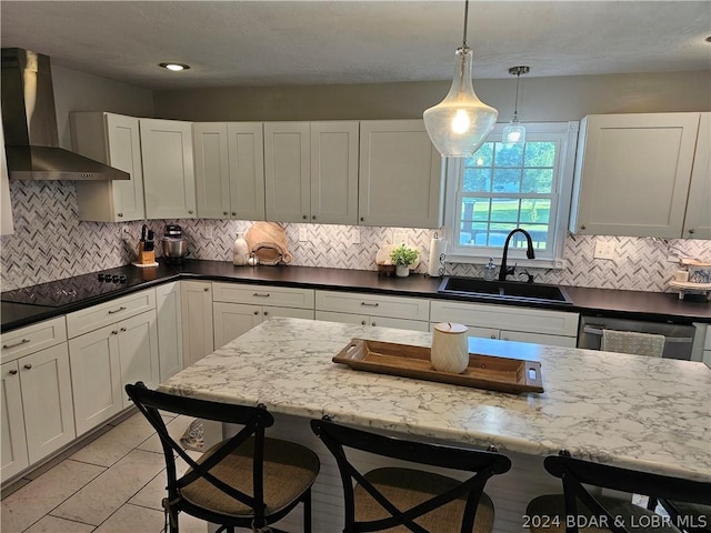 kitchen featuring hanging light fixtures, black electric cooktop, a kitchen bar, wall chimney exhaust hood, and sink