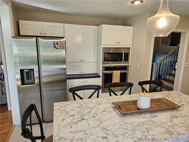 kitchen featuring stainless steel appliances, white cabinetry, pendant lighting, and light stone counters