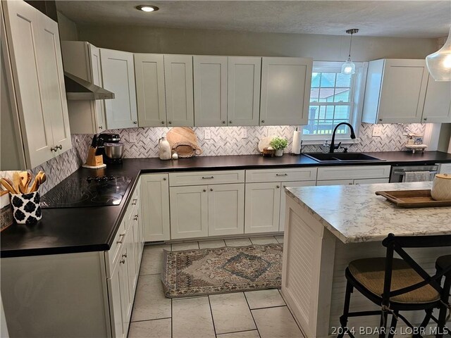 kitchen with wall chimney exhaust hood, pendant lighting, black electric cooktop, white cabinetry, and sink