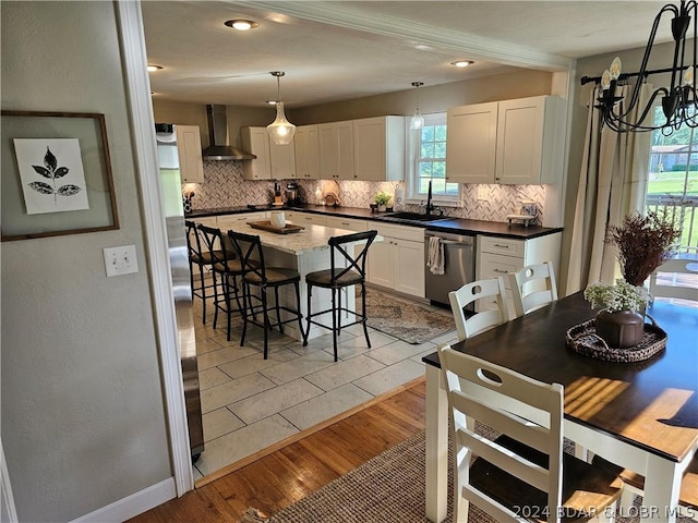 kitchen with wall chimney exhaust hood, pendant lighting, white cabinets, appliances with stainless steel finishes, and sink