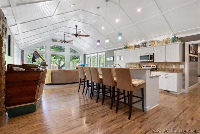 kitchen with a kitchen island with sink, appliances with stainless steel finishes, a kitchen bar, white cabinets, and tasteful backsplash