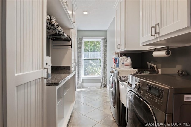 clothes washing area with washing machine and dryer, cabinets, and light tile patterned floors