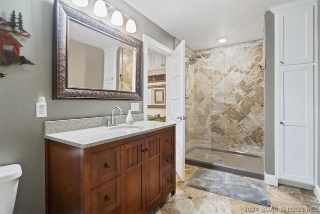 bathroom featuring a tile shower, vanity, and toilet