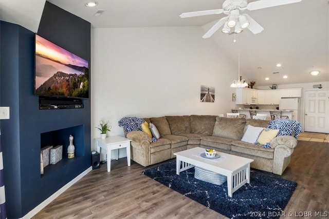 living room with ceiling fan with notable chandelier, hardwood / wood-style flooring, and vaulted ceiling