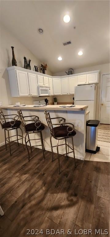 kitchen featuring dark hardwood / wood-style flooring, white appliances, vaulted ceiling, white cabinets, and a breakfast bar area