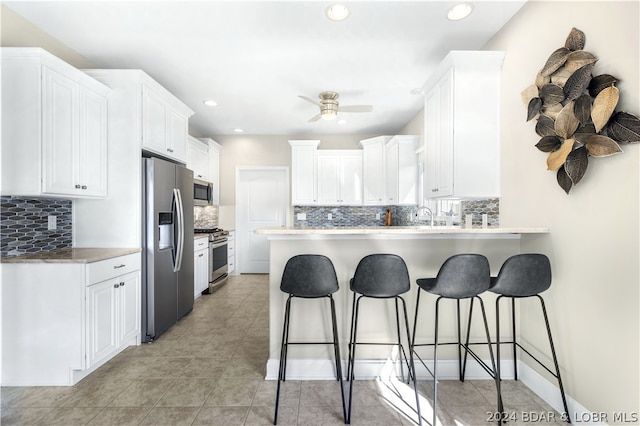 kitchen with a kitchen bar, kitchen peninsula, white cabinetry, and stainless steel appliances