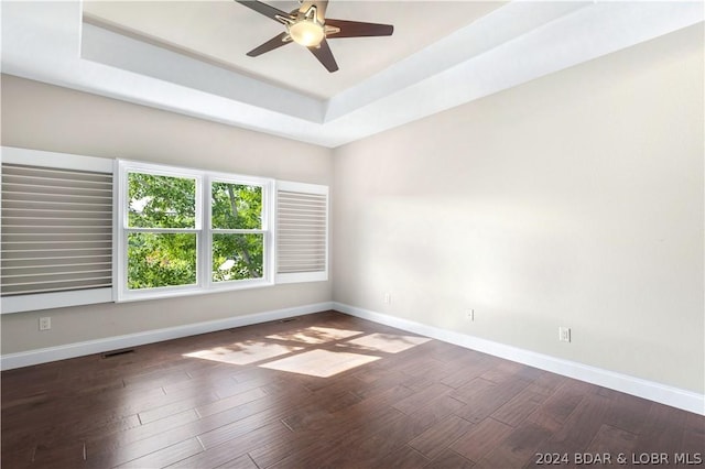 spare room with dark hardwood / wood-style flooring, a tray ceiling, and ceiling fan