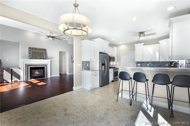 kitchen featuring decorative backsplash, appliances with stainless steel finishes, decorative light fixtures, white cabinets, and a breakfast bar area