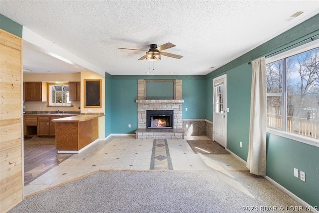 unfurnished living room with a textured ceiling, ceiling fan, light tile patterned floors, and a stone fireplace