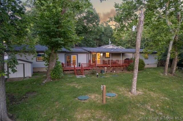 back house at dusk with a lawn, a wooden deck, and a storage shed