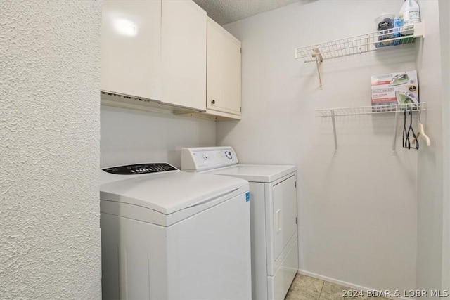 clothes washing area featuring washer and dryer, a textured ceiling, and cabinets