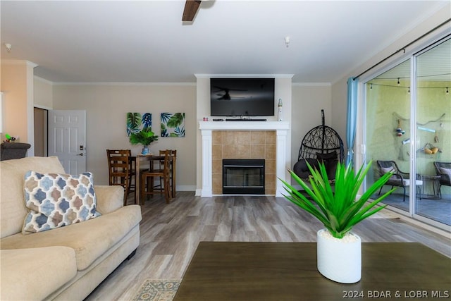 living room with hardwood / wood-style floors, ceiling fan, crown molding, and a tiled fireplace