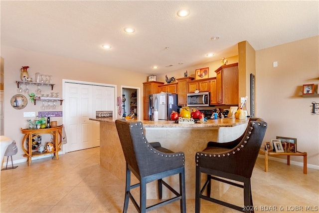 kitchen featuring a kitchen breakfast bar, kitchen peninsula, stainless steel appliances, and light tile patterned floors