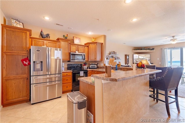 kitchen featuring a kitchen bar, light tile patterned floors, a textured ceiling, stainless steel appliances, and kitchen peninsula