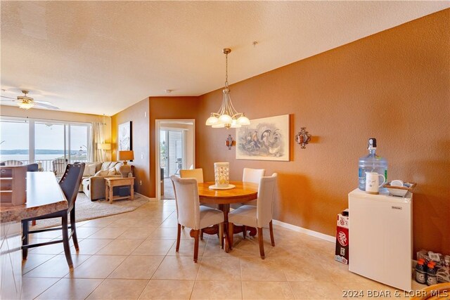 tiled dining room with ceiling fan with notable chandelier, a water view, and a textured ceiling