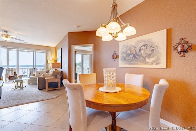 dining space featuring ceiling fan with notable chandelier, a water view, and light tile patterned floors