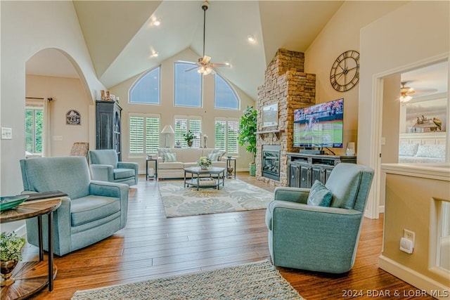 living room featuring high vaulted ceiling, ceiling fan, wood-type flooring, and a stone fireplace