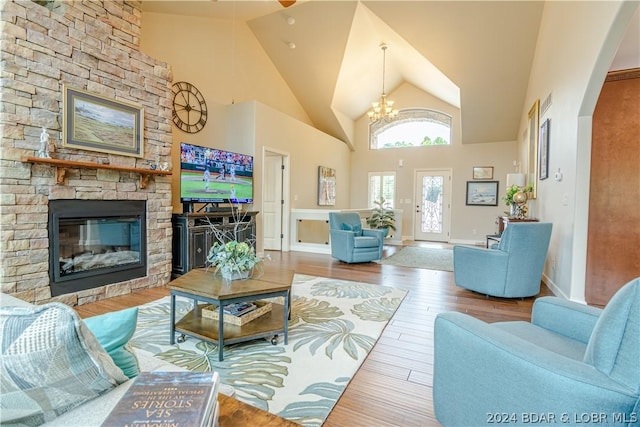 living room featuring an inviting chandelier, high vaulted ceiling, wood-type flooring, and a stone fireplace