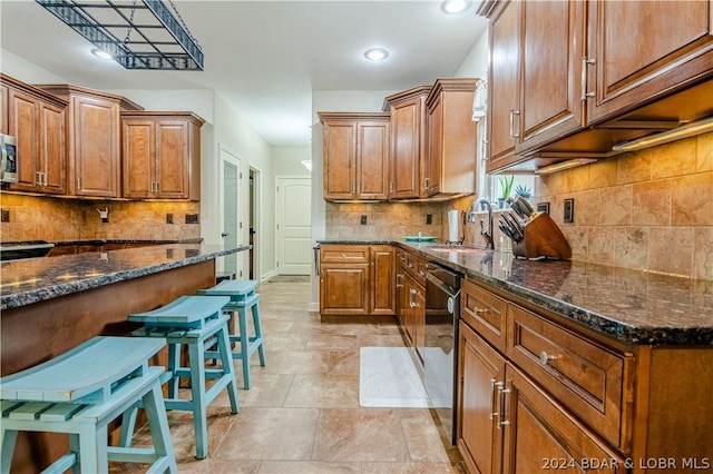 kitchen with dark stone counters, a kitchen breakfast bar, dishwasher, and sink