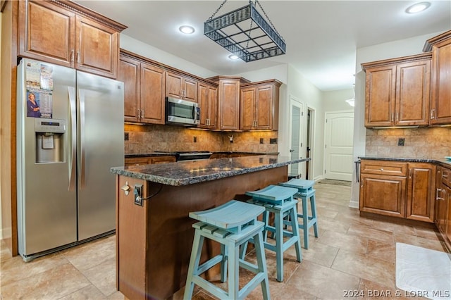 kitchen with a kitchen breakfast bar, stainless steel appliances, dark stone counters, decorative backsplash, and a kitchen island