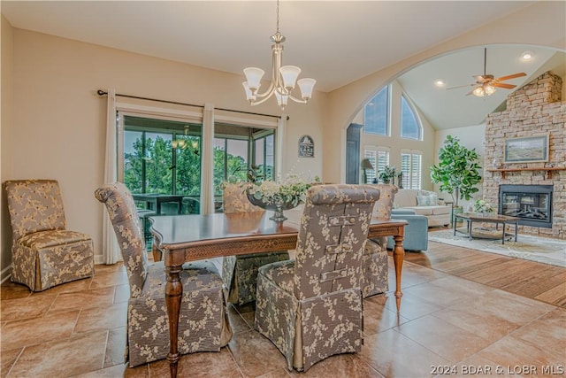 dining area with ceiling fan with notable chandelier, a fireplace, and vaulted ceiling