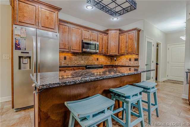 kitchen featuring a center island, stainless steel appliances, tasteful backsplash, a kitchen bar, and dark stone counters