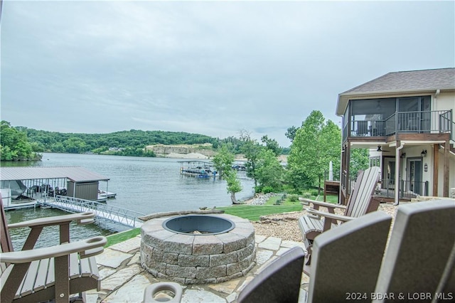 view of patio / terrace with a boat dock, a water view, an outdoor fire pit, and a sunroom