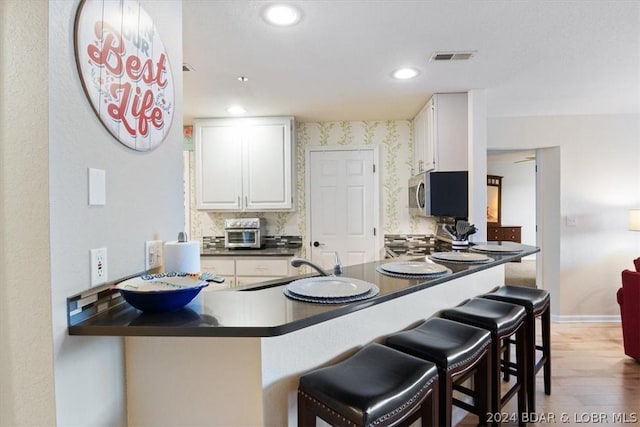 kitchen featuring a kitchen breakfast bar, kitchen peninsula, dark wood-type flooring, decorative backsplash, and white cabinets