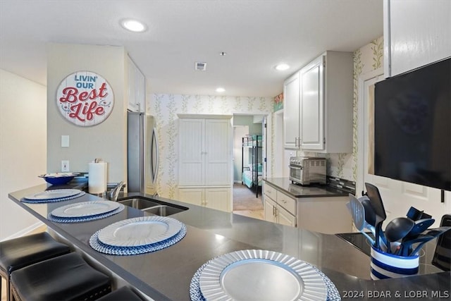 kitchen with sink, white cabinetry, kitchen peninsula, and stainless steel refrigerator