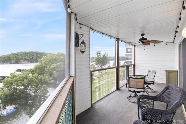 sunroom with ceiling fan and a water view