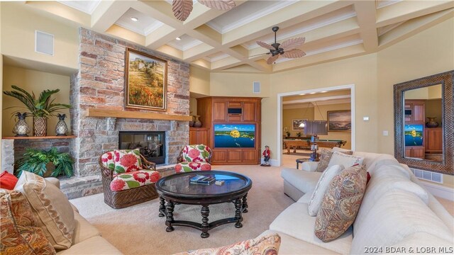 carpeted living room featuring ceiling fan, beamed ceiling, a high ceiling, coffered ceiling, and a stone fireplace