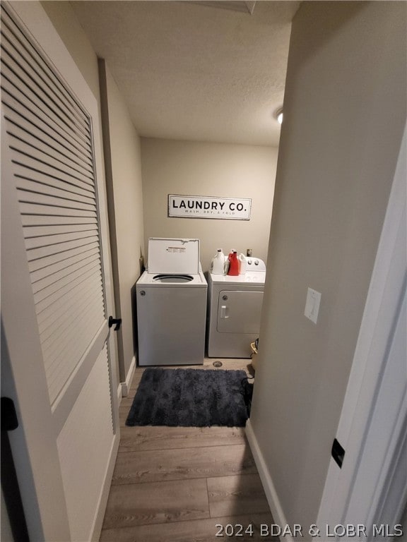 clothes washing area featuring separate washer and dryer, a textured ceiling, and wood-type flooring